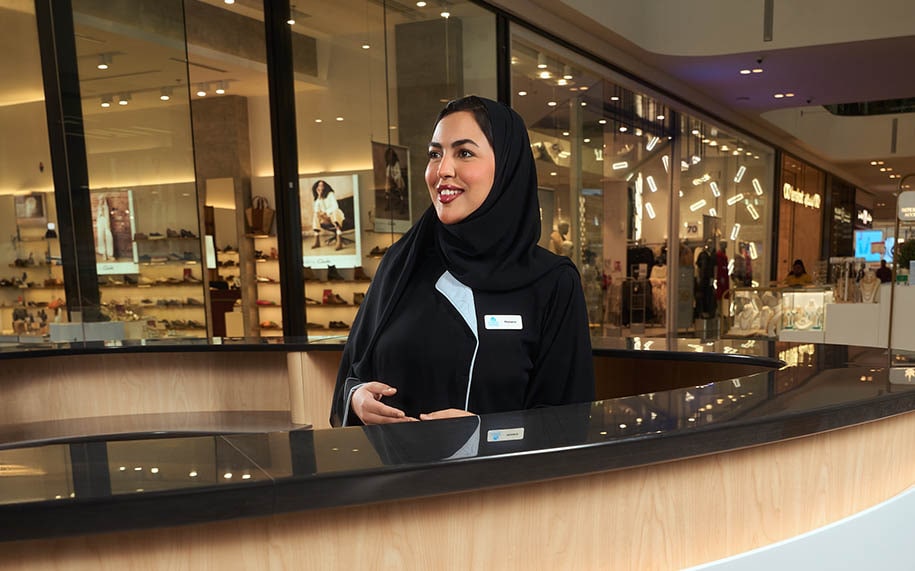 An arab woman smiling at the customers in a mall, standing behind the customer service desk